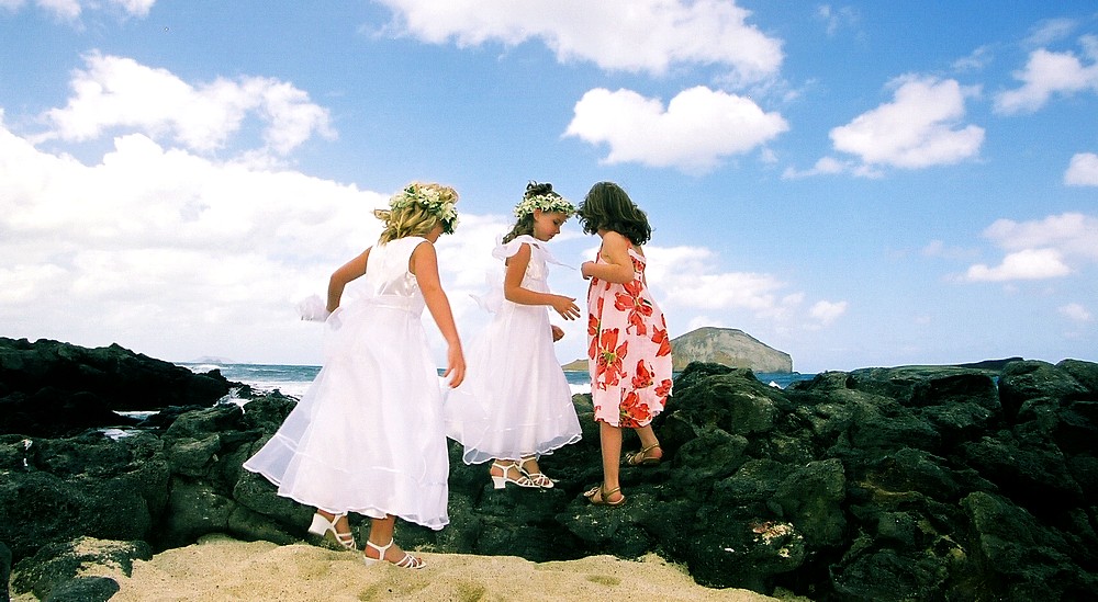 flower girls play on the lava rocks next to the weddign of Hawaii
