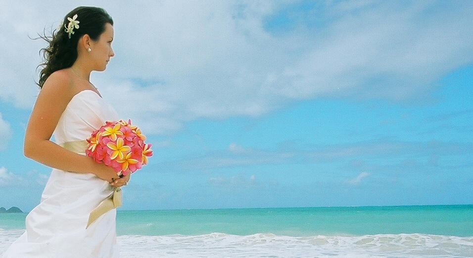 bride looking over the ocean with her pink and yellow bouquet