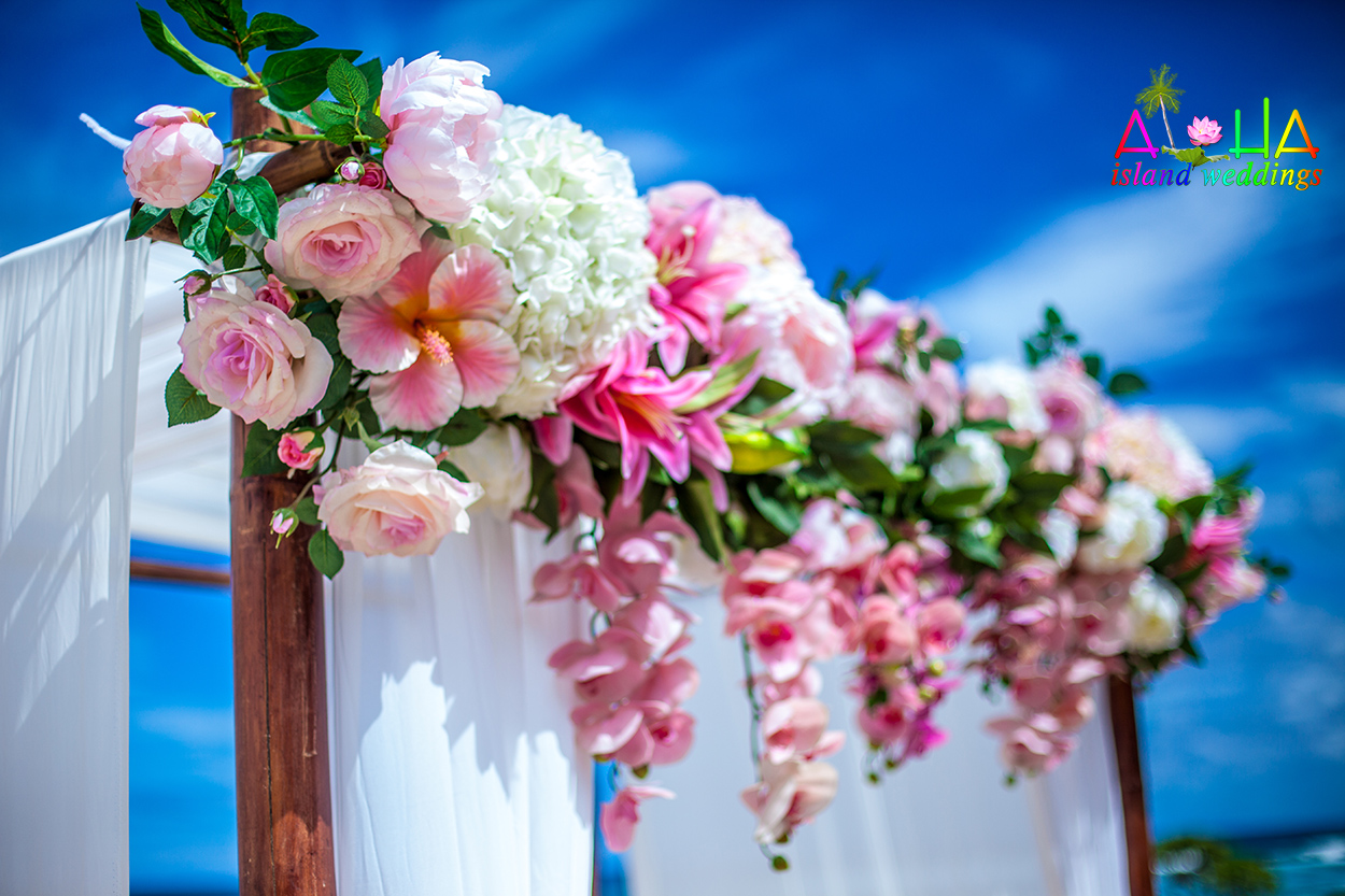 Close-up of pink plumerias, roses and hydrangeas on a dark bamboo wedding arch