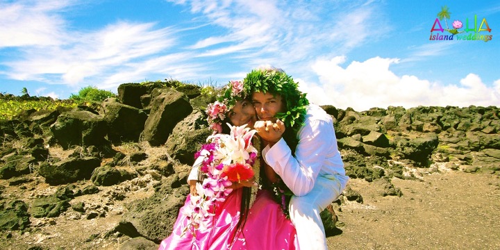 Paul and Dewi in flower leis smiling together by the rocks