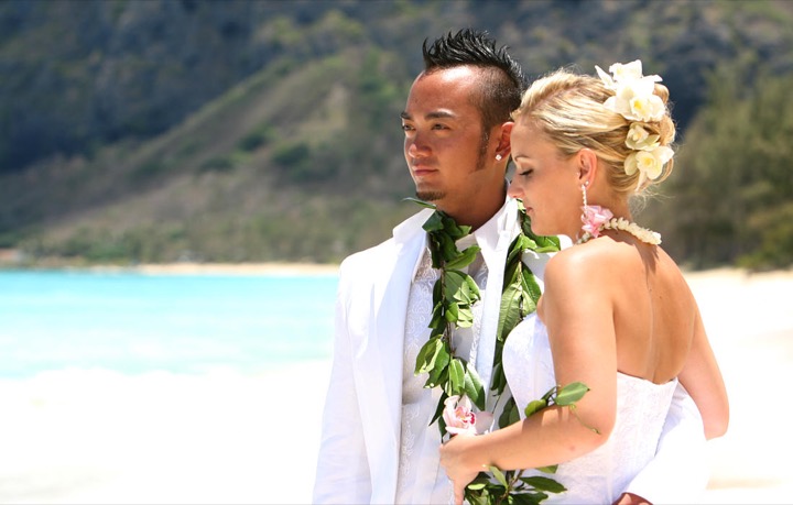 Chris and Angela embracing on the beach with the turquoise ocean behind