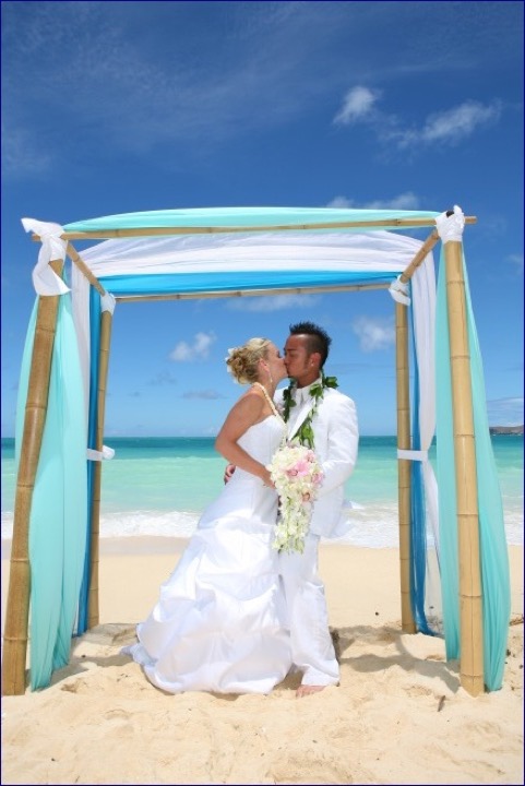 The couple framed by the turquoise draped arch