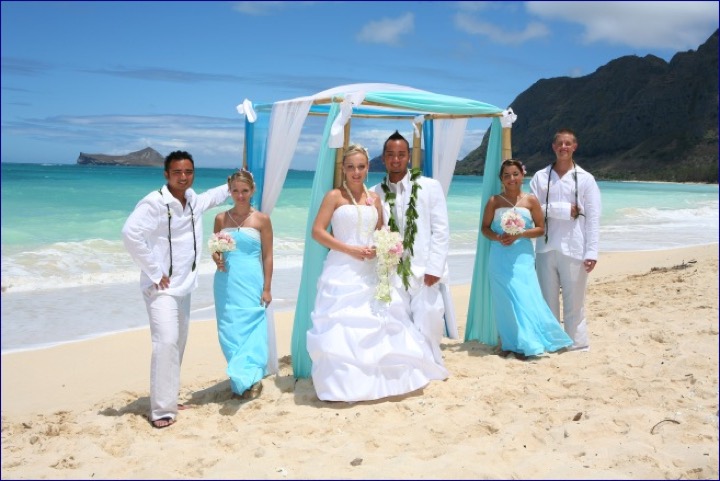 The bridal party lined up on the beach in front of the arch