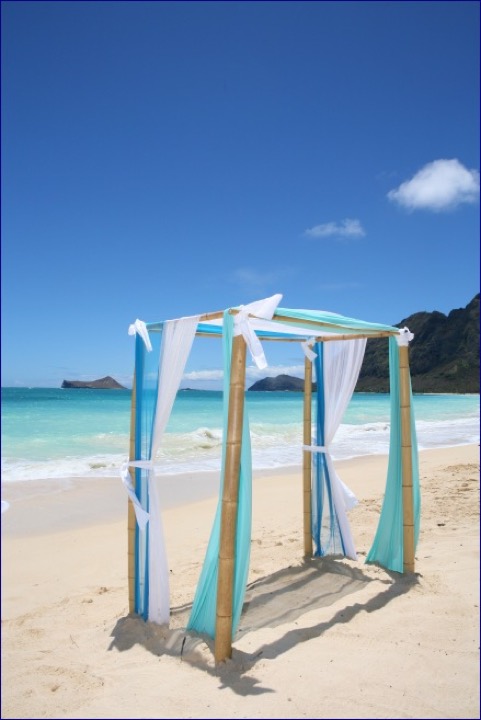 Turquoise and white draped bamboo arch on the white sand by the ocean