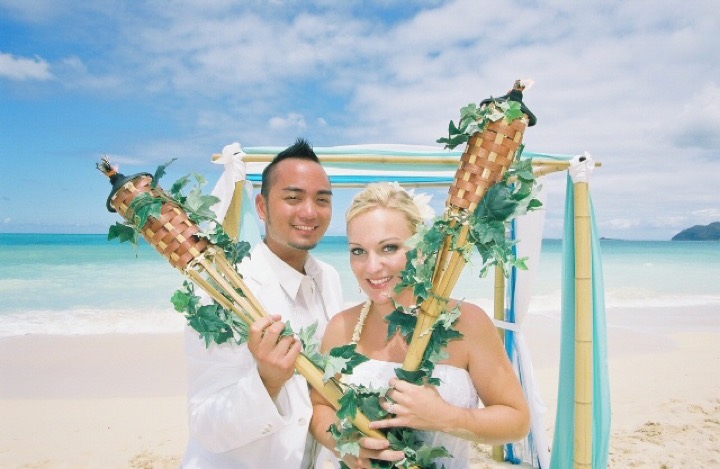 Angela and Chris holding flower-topped bamboo tiki torches