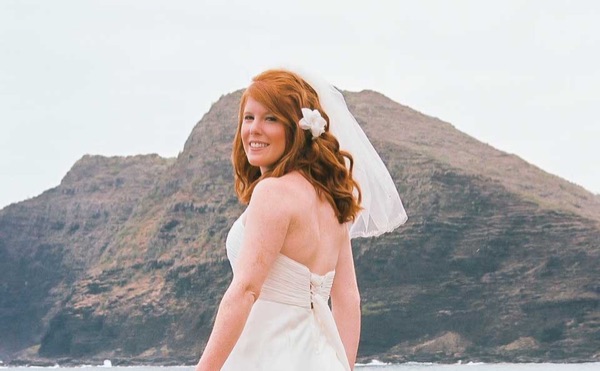 Ashley with her orange bouquet by the lava rocks, smiling