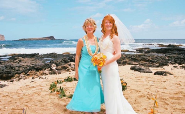 Ashley and her groom with family on the beach, under a blue sky