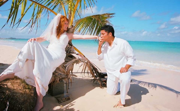 Ashley and her groom under a palm tree at Lanikai, in the sunshine
