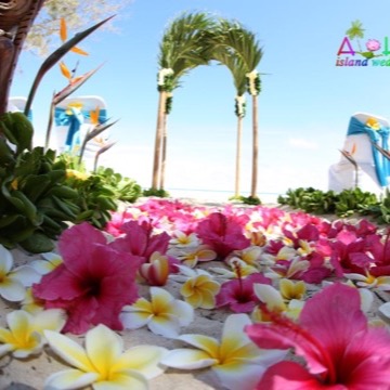 A starfish, a carved tiki and pink hibiscus petals on the sand by palm trees