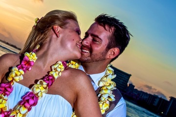 A couple in pink and yellow plumeria leis kissing at sunset in Waikiki