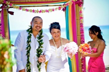 Bride and groom under a draped beach arch in leis