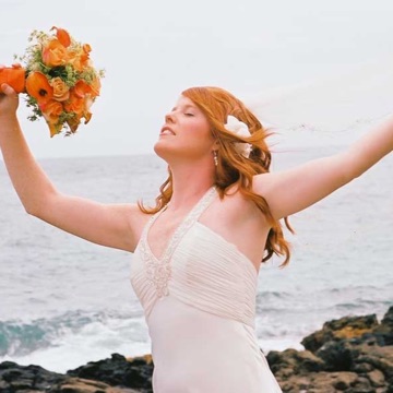 Ashley raising her bouquet with joy by the ocean