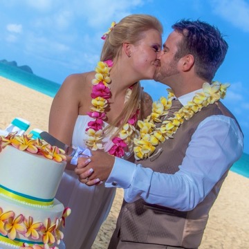 A couple from Germany kissing beside their plumeria wedding cake on the beach