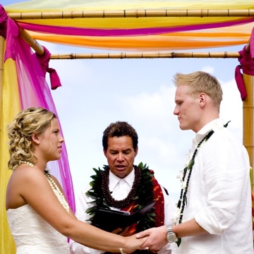 Natasha and Tyson under a pink and yellow arch by the sea