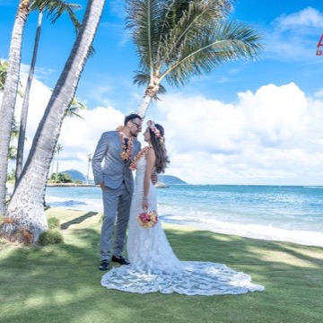 Newlyweds kiss under the palms by the beach at Waialae