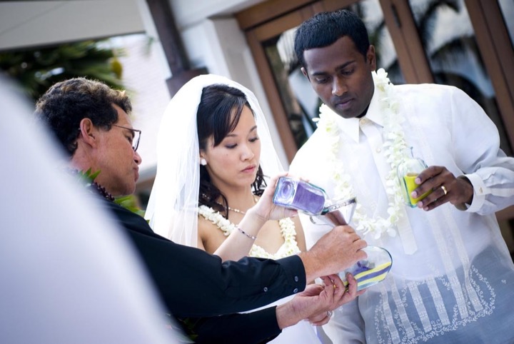 A couple pouring colored Hawaiian sand together with Rev. Kimo
