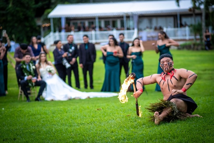Samoan fire knife dancer with face paint performing on the lawn for the bride and groom at Loulu Palms estate