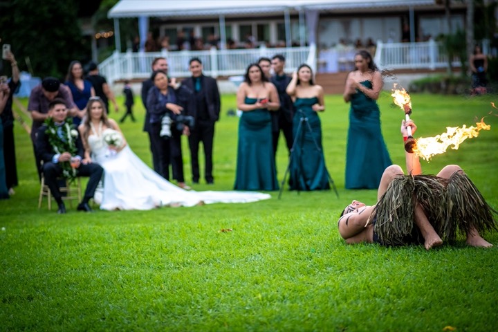 Fire dancer lying on the grass spinning a flaming knife in front of the couple at their Loulu Palms estate wedding