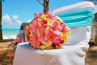 Yellow and pink plumeria bouquet resting on a chair with a turquoise sash