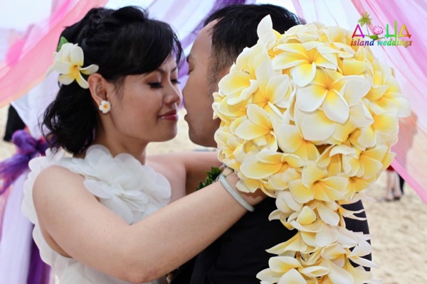 Bride holding a teardrop yellow plumeria bouquet on the beach