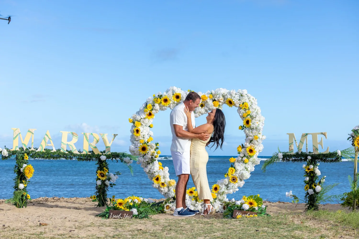 A heart of white and yellow roses with sunflowers and MARRY ME letters on Waialae Beach