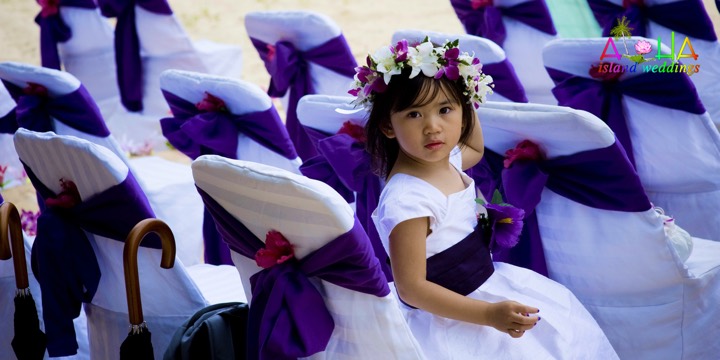Flower girl in a purple and white orchid head lei on the beach chairs