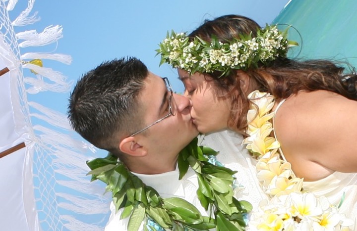 Bride in a green and white baby's breath haku lei sharing a kiss