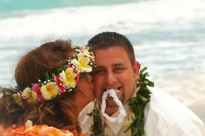Bride in a pink and yellow haku lei kissing the groom