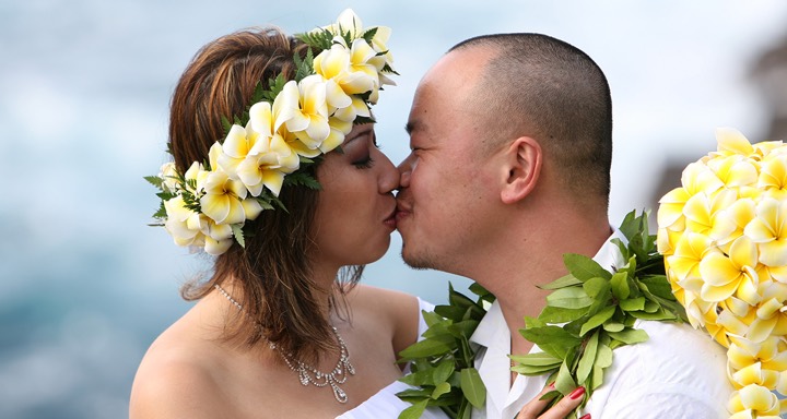 Bride in a yellow plumeria haku lei kissing her husband
