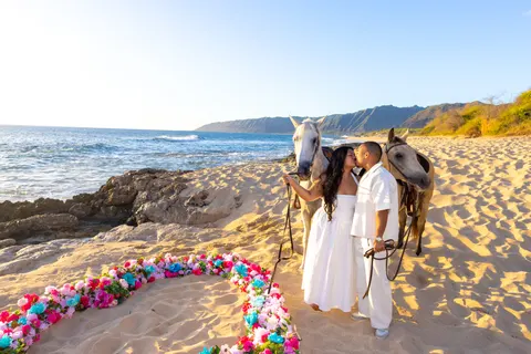 Couple and horses beside pink and blue flower heart, at a horseback proposal on Oahu