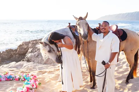 Couple greeting their horses on the beach, at a horseback proposal on Oahu