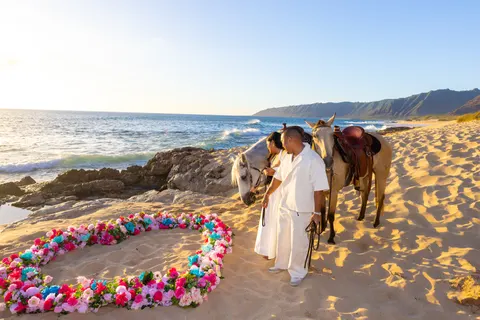 Couple hugging beside their horses on the sand, at a horseback proposal on Oahu
