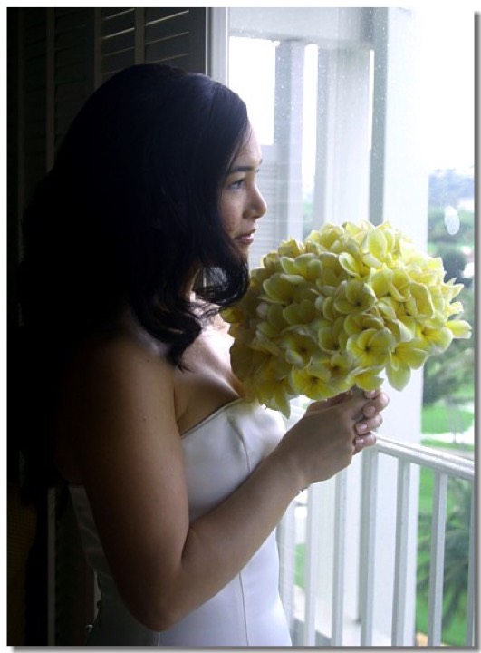 Bride with a yellow plumeria bouquet by the window of her Kahala Resort room