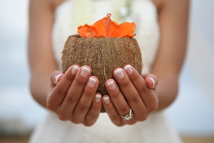 Bride holding a coconut decorated with a hibiscus flower at a Hawaii beach wedding