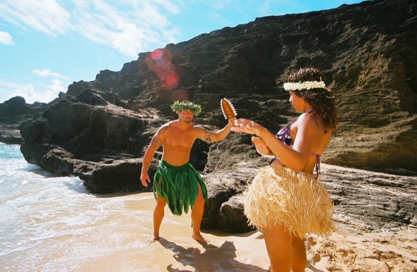 Jamillah and Brandon in grass skirts and haku leis at the cove, having fun