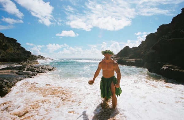 Jamillah and Brandon in grass skirts and haku leis at the cove, in the afternoon light