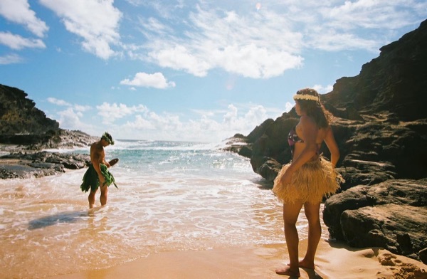 Jamillah and Brandon in grass skirts and haku leis at the cove, close together