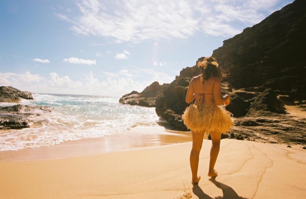 Jamillah and Brandon in grass skirts and haku leis at the cove, in the bright sun