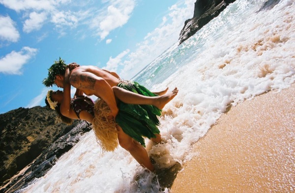 Jamillah and Brandon in grass skirts and haku leis at the cove, in a happy moment