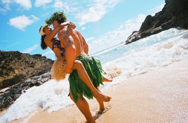 Jamillah and Brandon in grass skirts and haku leis at the cove, side by side