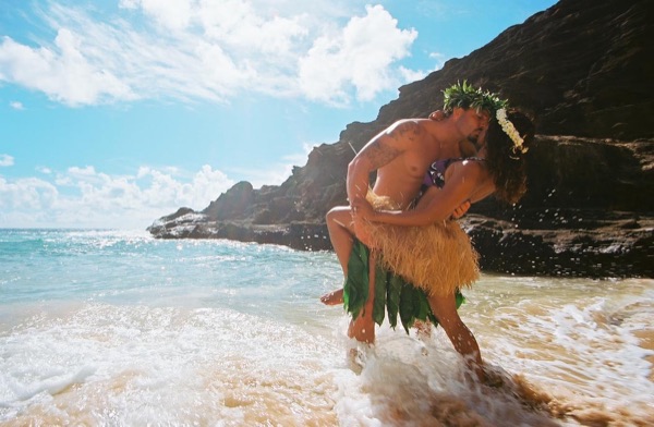 Jamillah and Brandon in grass skirts and haku leis at the cove, laughing together