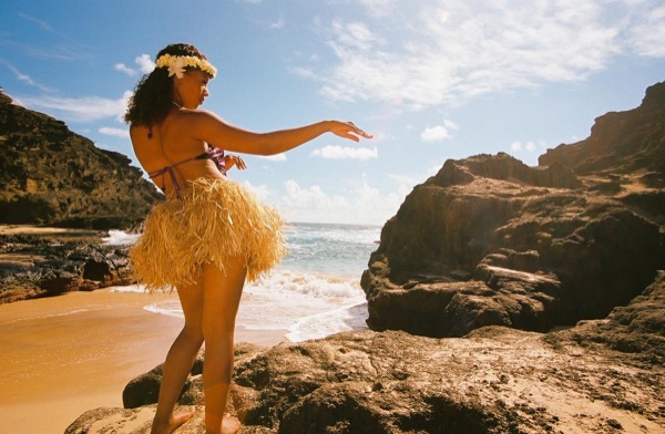 Jamillah and Brandon in grass skirts and haku leis at the cove, in the breeze