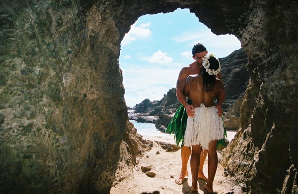 Jamillah and Brandon in a lava tube cave by the beach, under a blue sky