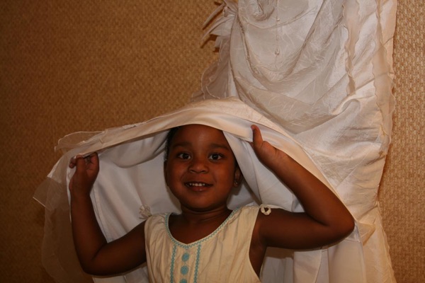 The little flower girl playing under the bride's dress