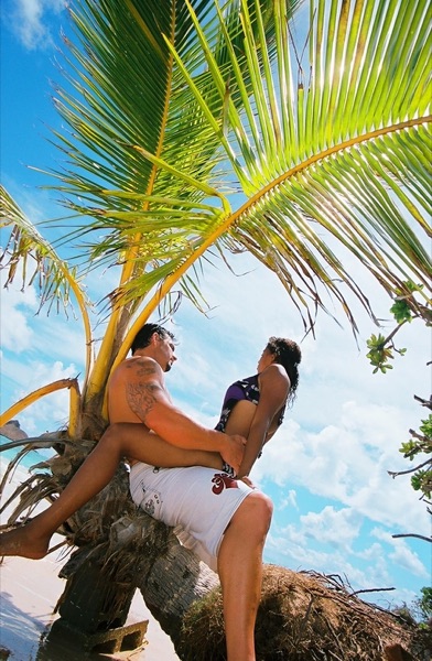 Jamillah and Brandon under a leaning palm at Lanikai, looking at each other