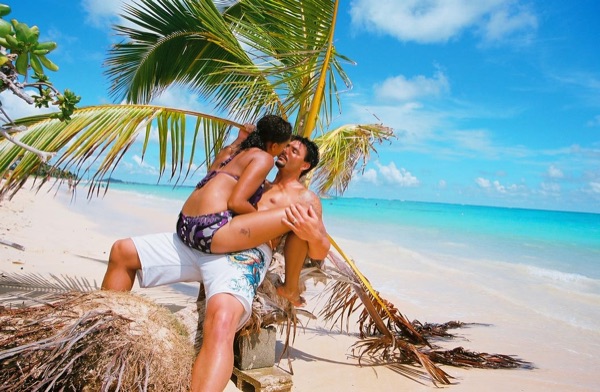 Jamillah and Brandon under a leaning palm at Lanikai, in the sunshine