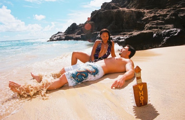 Brandon lying on the sand as the waves wash in at the cove, under a blue sky