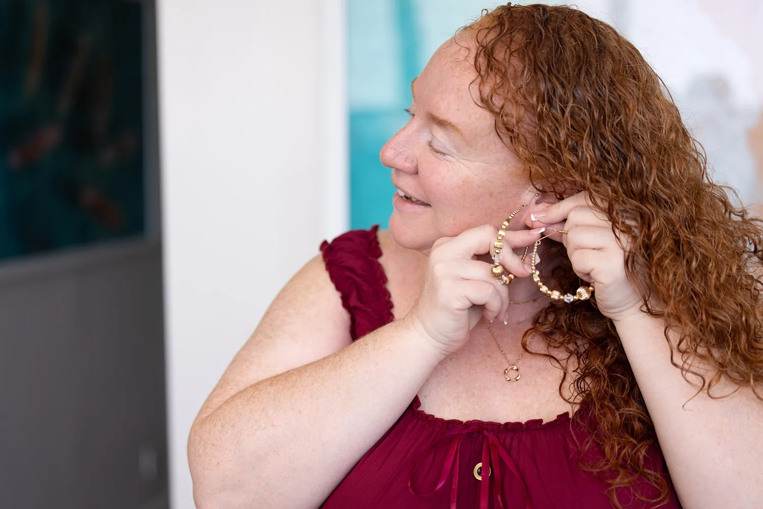 A bridesmaid in wine red putting on her earrings