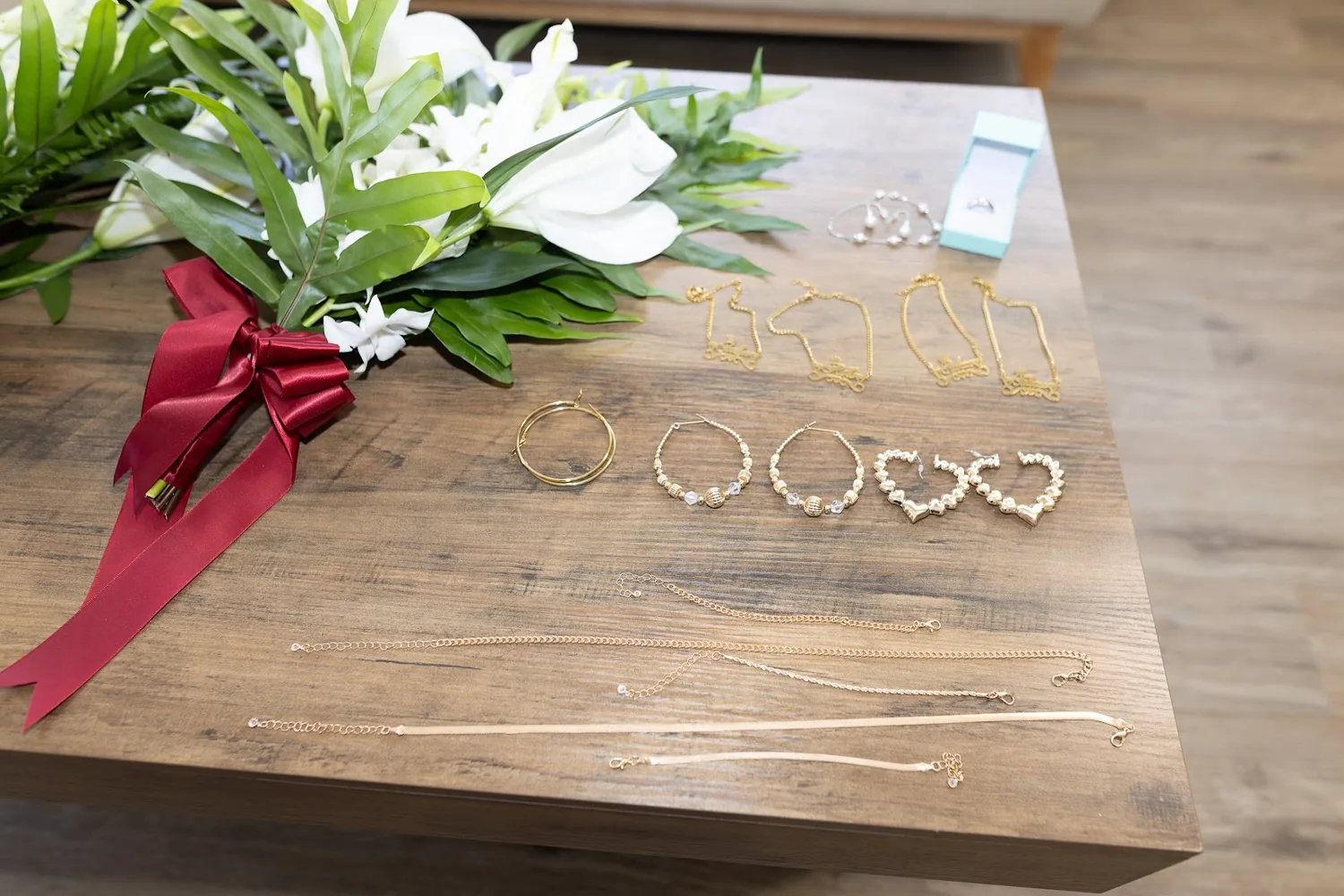 White lily bouquets tied with wine red ribbon beside the jewelry