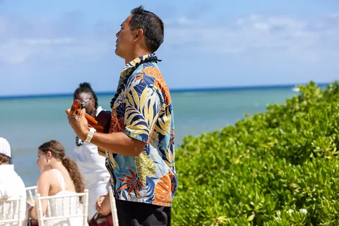 A musician playing the ukulele by the ocean during the ceremony
